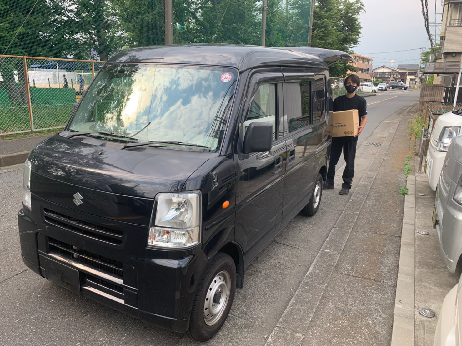 BURNING BROS.の配送ドライバーが荷物を持って軽貨物車両の横に立つ実際の現場